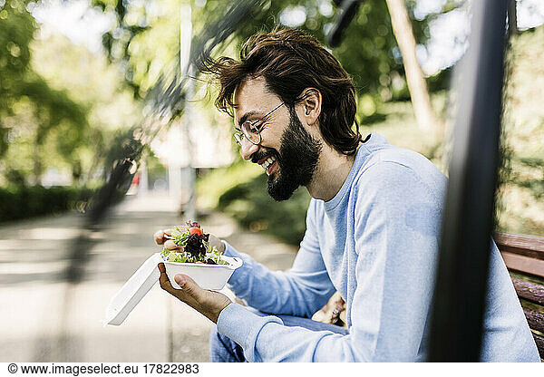 Smiling bearded man with salad sitting in park