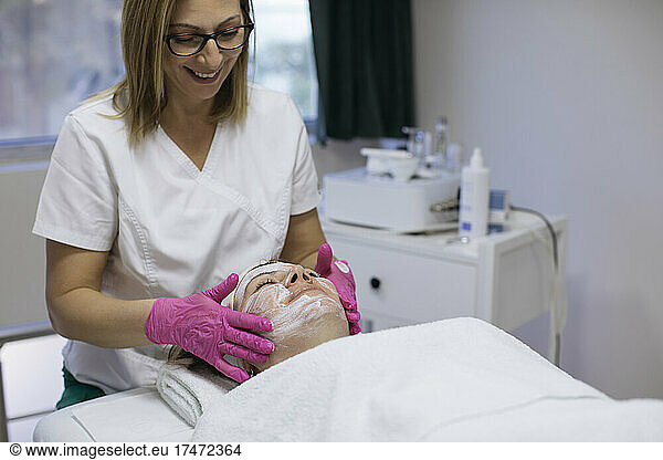 Smiling beautician applying moisturizer to woman in salon