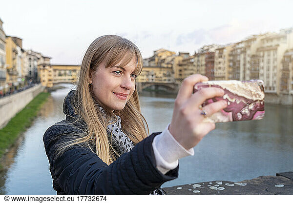 Smiling beautiful woman with bangs taking selfie through smart phone