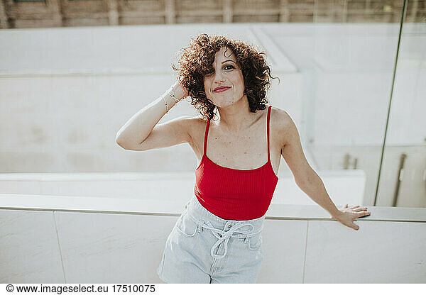 Smiling beautiful woman with curly hair standing by retaining wall in city