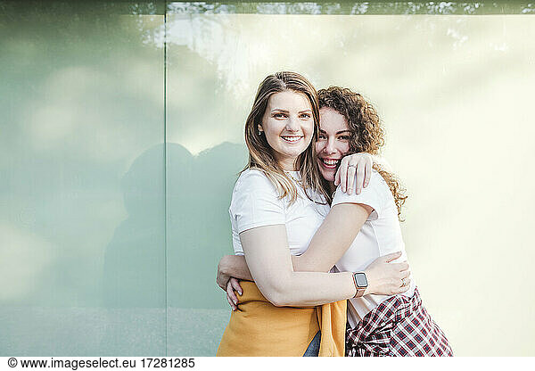 Smiling beautiful women hugging each other against wall