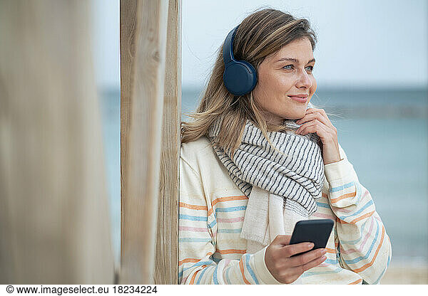 Smiling beautiful young woman holding smart phone listening to music at beach
