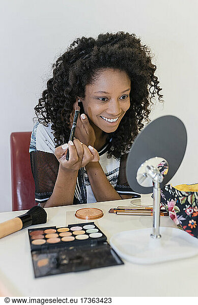 Smiling beauty expert holding make-up brush while looking at mirror