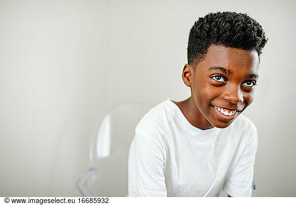 Smiling black boy with big brown eyes clear acrylic chair looking up
