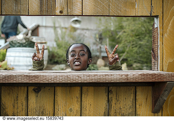 Smiling black girl with chin on ledge making peace signs at nursery