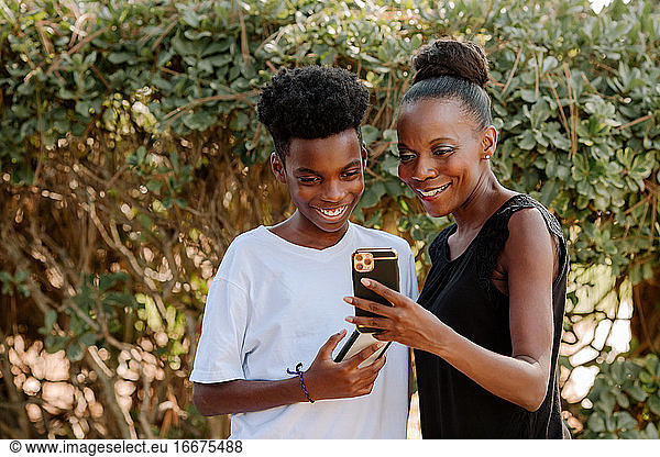 Smiling Black mom and preteen son looking at cellphones together