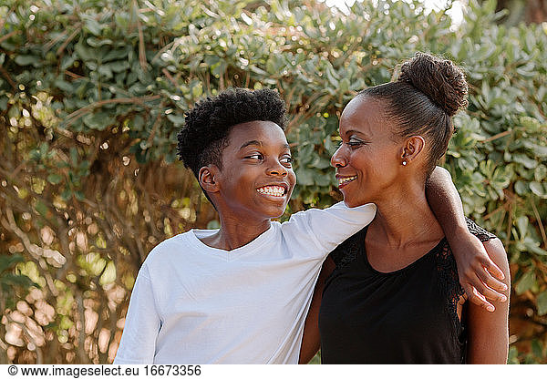 Smiling Black preteen boy with arm around shoulder of happy mom