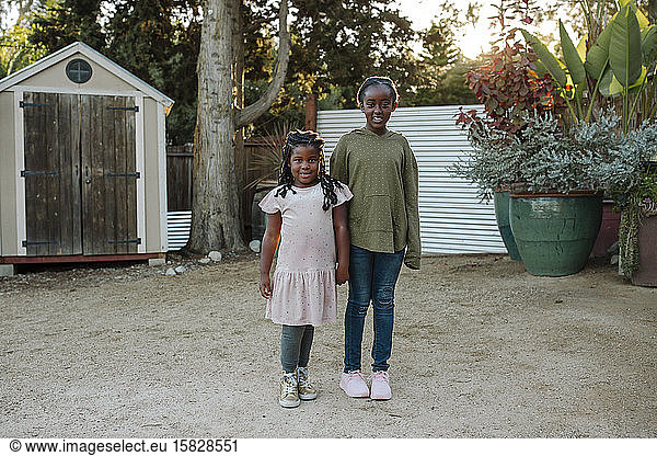 Smiling black sisters standing in garden with huge plants