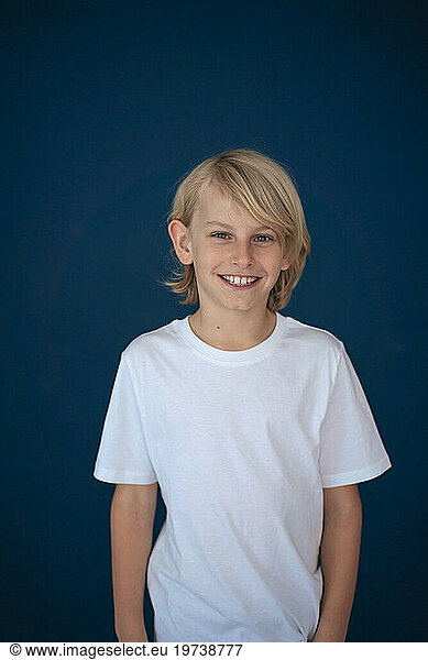 Smiling blond boy standing against blue background