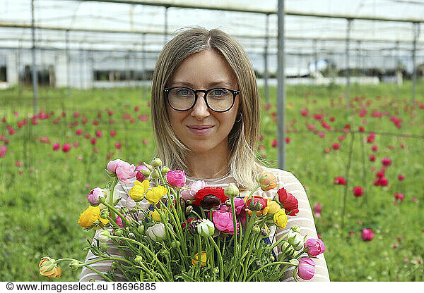Smiling blond farmer with bunch of Ranunculus flowers in greenhouse