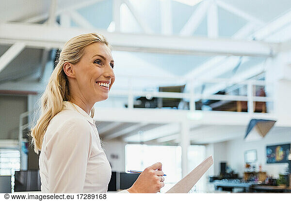 Smiling blond female professional with documents in creative office looking away