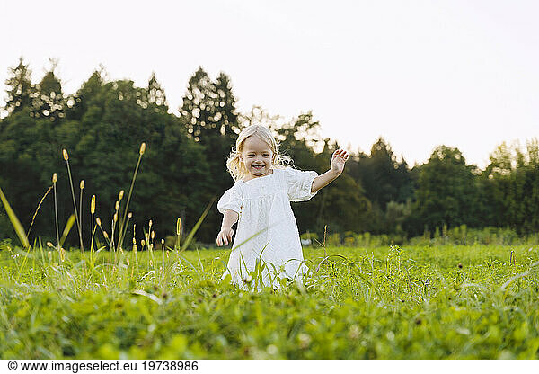 Smiling blond girl running in front of trees