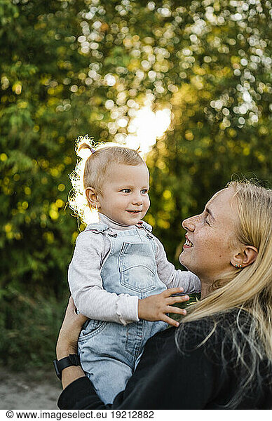 Smiling blond woman carrying daughter in park