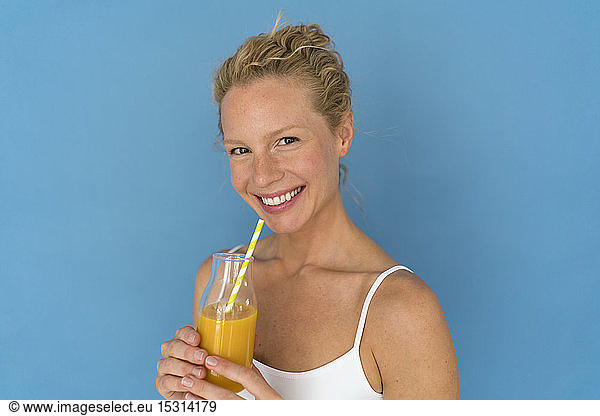 Smiling blond woman drinking juice  blue background