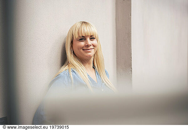 Smiling blond woman leaning on wall