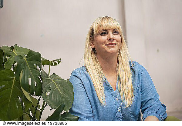Smiling blond woman sitting near plant