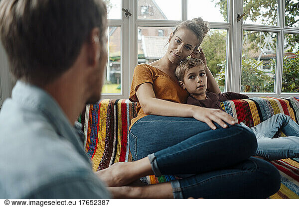 Smiling blond woman sitting with boy on sofa looking at man