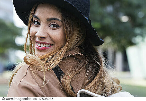 Smiling blond woman wearing hat looking over shoulder