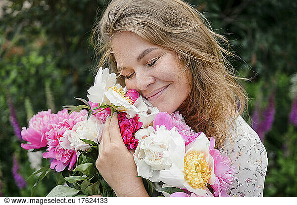 Smiling blond woman with eyes closed hugging flowers