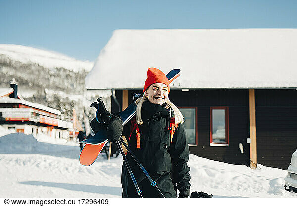Smiling blond woman with ski standing at tourist resort