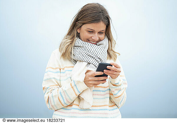 Smiling blond young woman using smart phone at beach