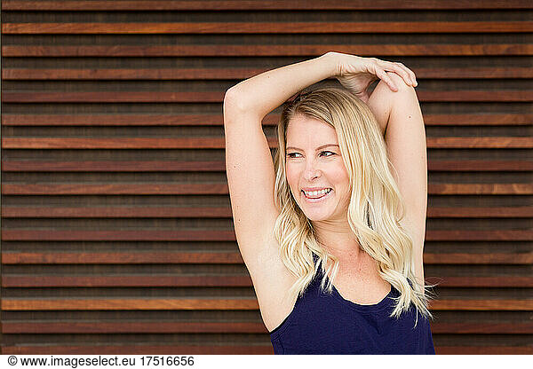 Smiling blonde woman stretching in front of wooden wall