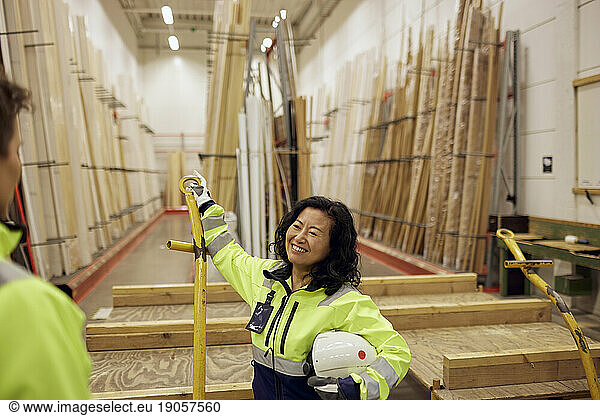 Smiling blue-collar worker discussing with colleague in lumber industry