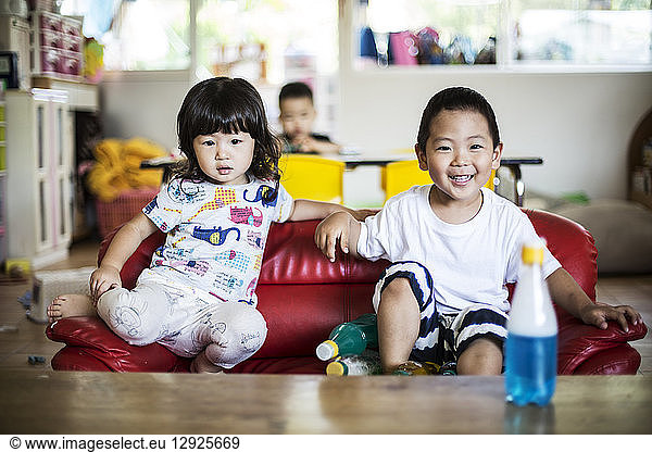 Smiling boy and girl sitting on red sofa in a Japanese preschool.