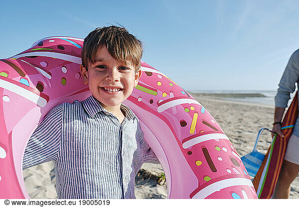 Smiling boy carrying inflatable swim ring at beach