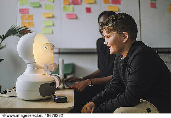 Smiling boy communicating with illuminated AI robot in innovation lab