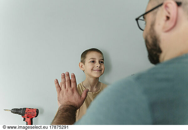 Smiling boy giving high-five to father in front of wall