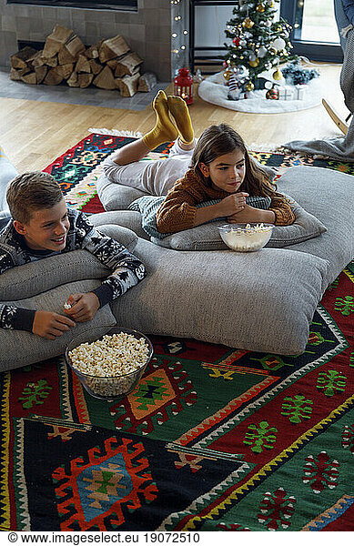 Smiling boy having popcorn by sister and watching TV at home
