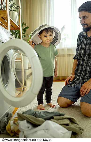 Smiling boy helping father washing clothes in machine at home