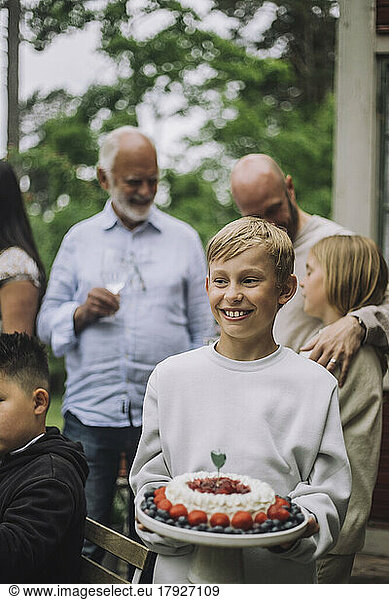 Smiling boy holding cake at birthday party