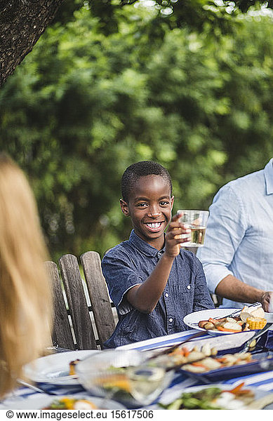 Smiling boy holding drinking glass while sitting with family in backyard during party