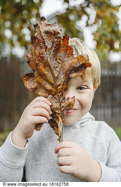Smiling boy holding dry leaf over face