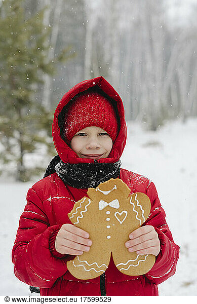 Smiling boy holding gingerbread cookie in snowy forest