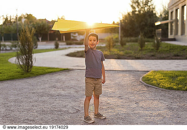 Smiling boy holding paper airplane and standing in park
