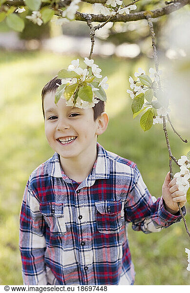 Smiling boy holding tree branch at back yard in springtime