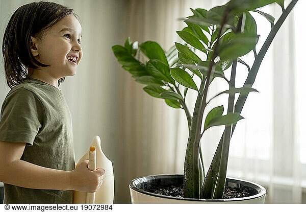 Smiling boy holding watering can by plants at home