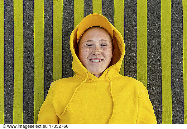 Smiling boy in yellow sweatshirt lying on road marking