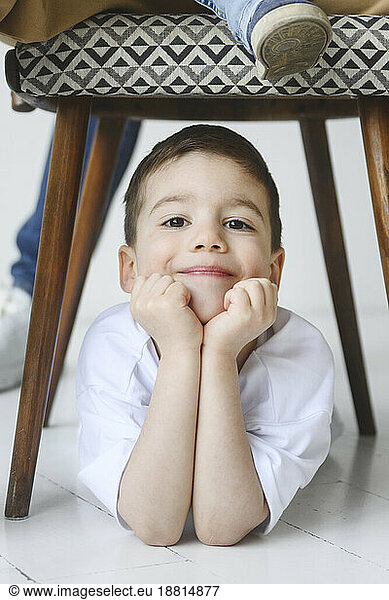 Smiling boy leaning on elbows under chair