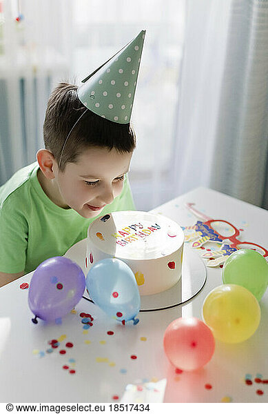 Smiling boy looking at birthday cake amidst balloons and confetti