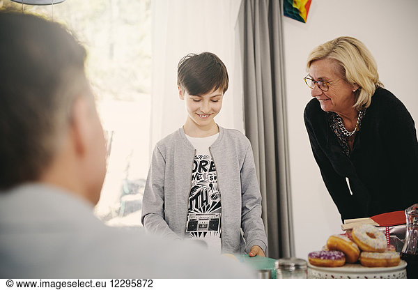 Smiling boy looking at birthday present while standing with grandmother at table