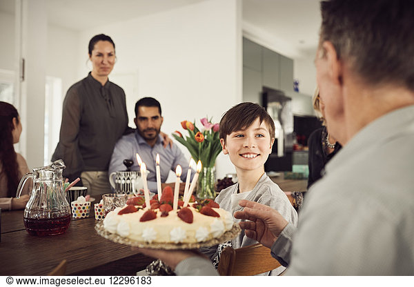 Smiling boy looking at grandfather holding birthday cake with family in party
