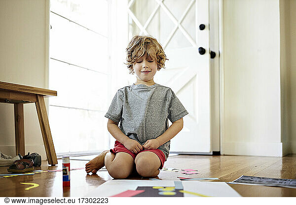 Smiling boy looking at paper art while sitting in living room at home