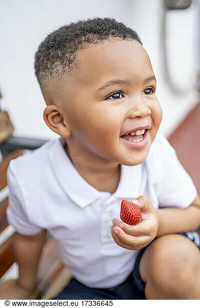 Smiling boy looking away holding strawberry