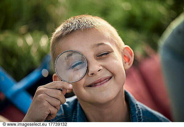 Smiling boy looking through magnifying glass on picnic