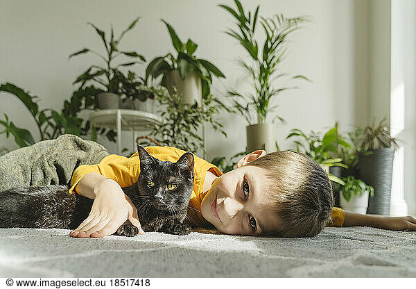 Smiling boy lying on carpet with black cat