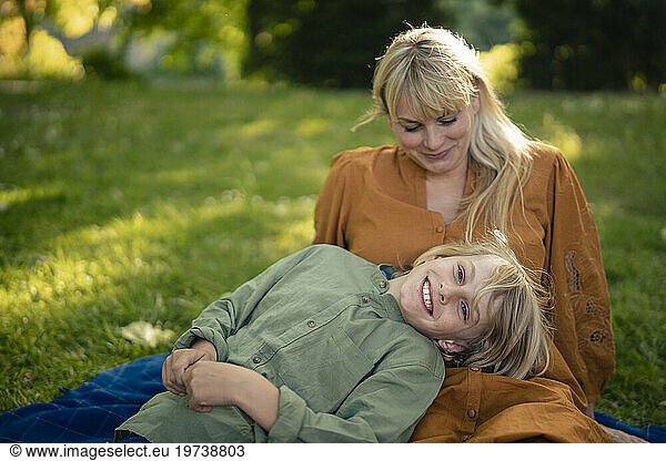 Smiling boy lying on mother's lap in park